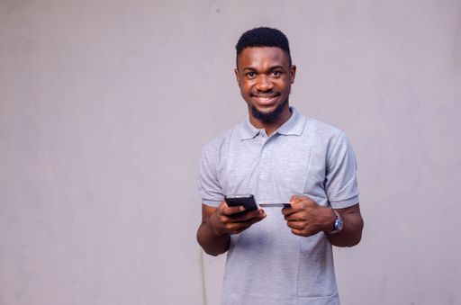 An African-American man using his card and his phone on a grey background