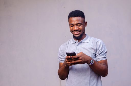 A cheerful African-American man using his phone on a grey background