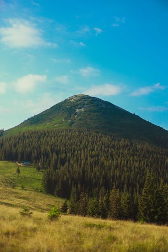 A vertical shot of hills covered in greenery under a blue cloudy sky in the countryside