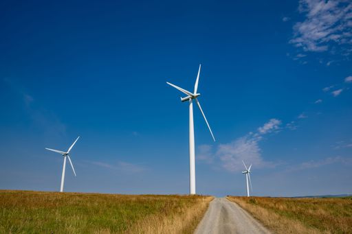 A beautiful shot of wind turbines, a dirt-road passing through wind farms under a blue sky