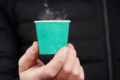 A closeup shot of a man's hand holding a turquoise paper cup with hot coffee