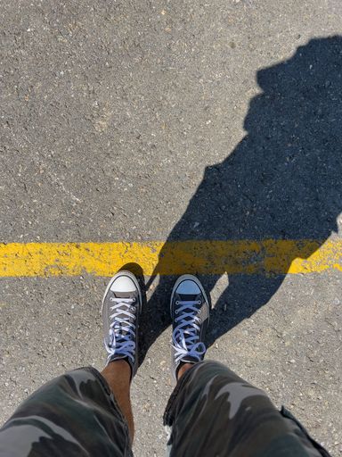 A vertical shot of a man's black sneakers next to an orange line on an asphalt road