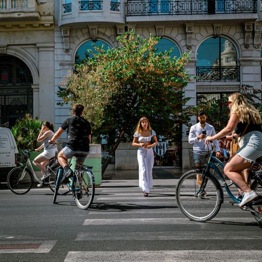A woman in white trousers walking across a busyValencia road with bicycles