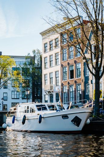 A vertical shot of a white yacht in Amsterdam canal with buildings in the background
