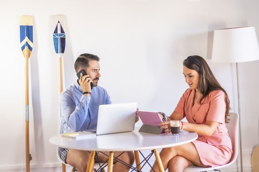 A male and a female discussing a project using a laptop and tablet while sitting around a table next to each other