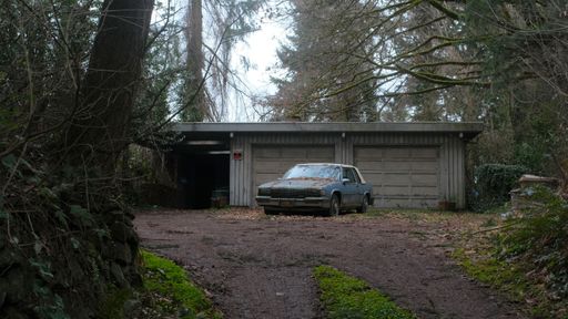 An old Cadillac parked in front of abandoned somewhat derelict home with a muddy road