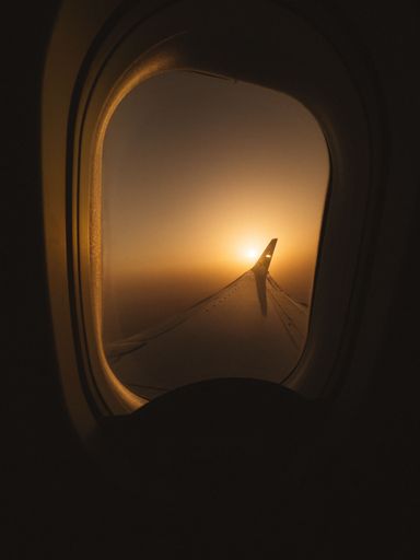 A vertical shot of a plane's wing appearing from the window with sunset view