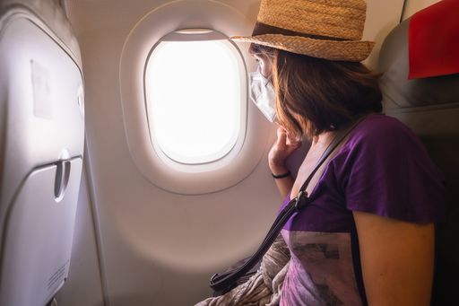 A female in a protective face mask looking out of an airplane window