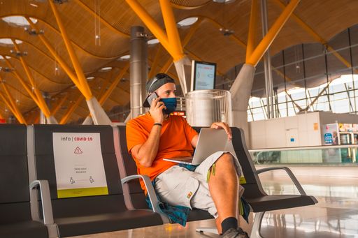 A young male wearing a face mask in the airport and talking on his phone - the new normal