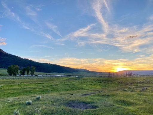 A beautiful cloudscape view in golden hour over green grassy valley, small lake and hills