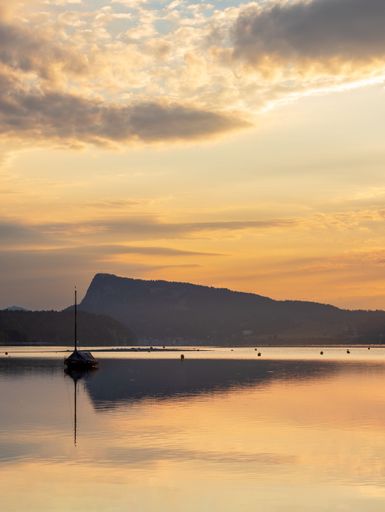 A scenic vertical shot of a boat at golden sunrise, on calm waters of Lac de Joux lake, Switzerland