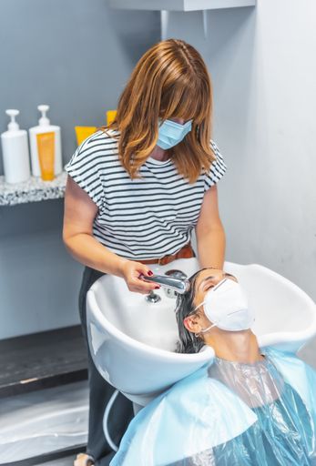 The new normal - a hairdresser washing the customer's hair, both wearing face masks