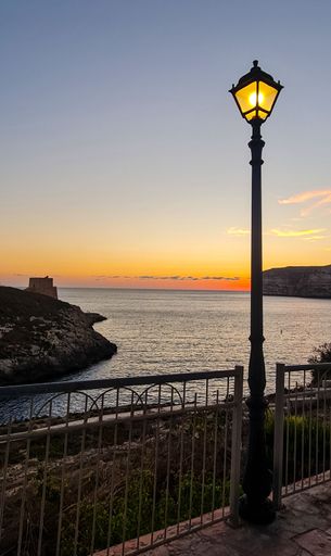 A vertical shot of illuminated lantern by fenced lakeshore during sunset