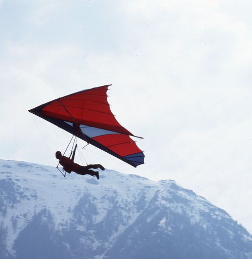 A closeup shot of a young man flying over the mountains with his parachute