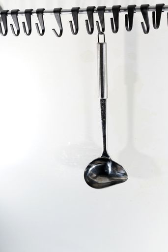 A vertical shot of a metal ladle hanging on a white wall