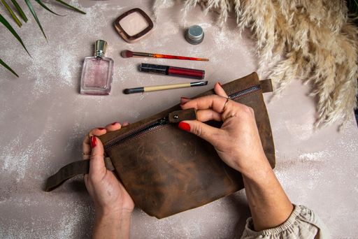 A top view of handmade leather red makeup bag on her hands with makeup kits on the table
