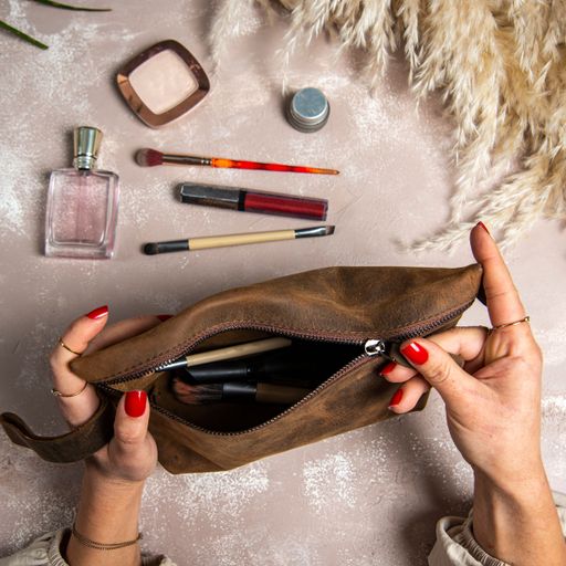 A top view of a woman opening a handmade leather makeup bag on her hands
