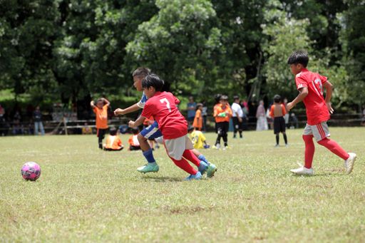 Asian Kids with red and blue uniforms playing football on the soccer field in Jakarta, Indonesia
