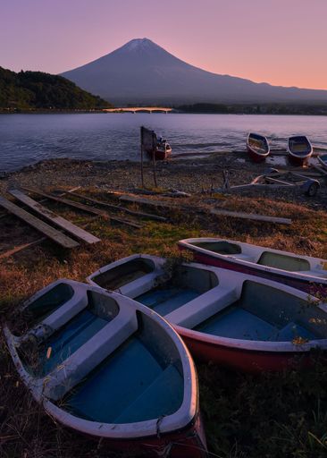 A scenic shot of a tranquil lake with moored boats near a mountain at sunset