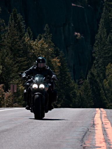 A vertical shot of a biker riding a motorcycle on the highway road near the Stone Hill on a sunny day