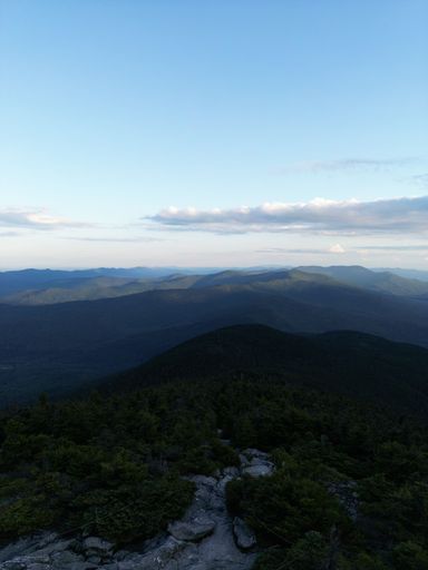 A vertical shot of mountain fields under a cloudy blue sky