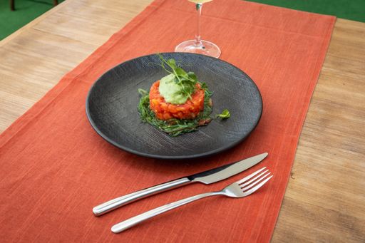 A closeup of a tomato tartare on chuka salad stuffed with avocado sauce served on a black plate