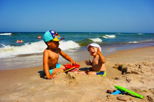Two young boys playing with toys on sand close by the water at a beach