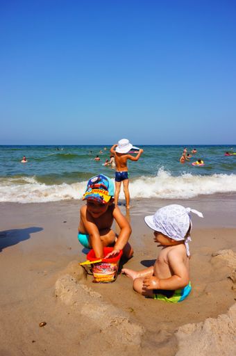 Two young boys playing with toys on sand close by the water at a beach