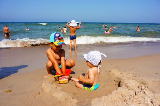 Two young boys playing with toys on sand close by the water at a beach