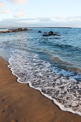 A vertical shot of the sea waves on a sandy beach at sunset in Kona, Hawaii
