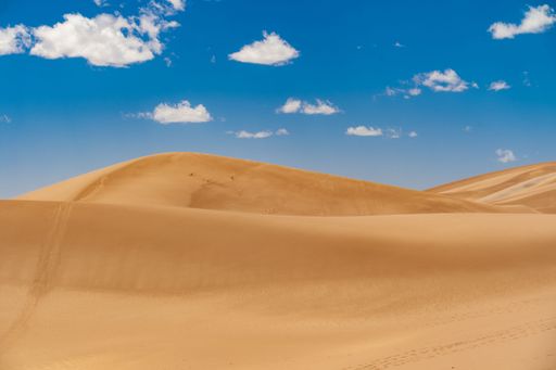 An aerial view of desert with sandy hills under blue bright sky