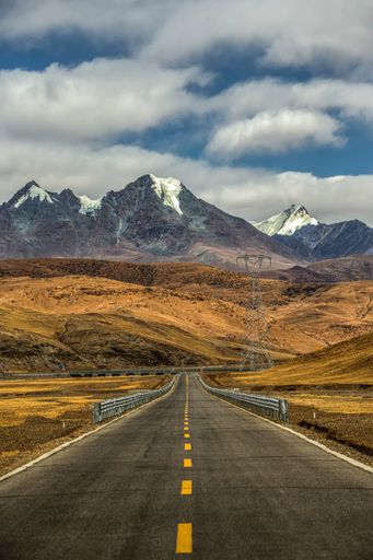 A vertical shot of a highway directed to snowy mountains in Saga Country, Xigaze, China