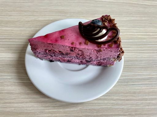 Closeup shot of a delicious raw blueberry cake with cream and chocolate on a white plate lying on a wooden table.