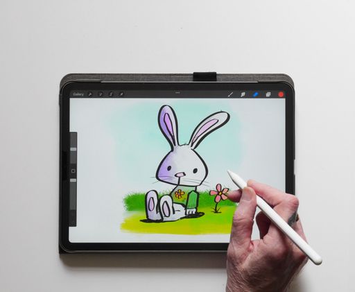 A person's hand drawing a cartoon Easter rabbit on an iPad Pro using an Apple Pencil