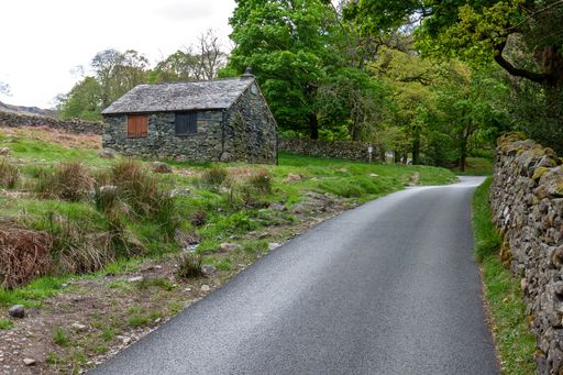 An empty asphalt road passing by a stone building surrounded by green trees