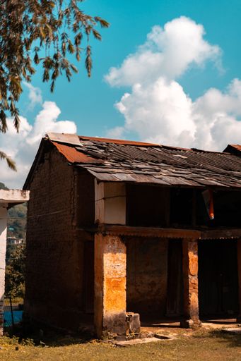 A vertical shot of an old house under blue cloudy sky in the Indian State of Himachal Pradesh