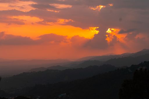 A scenic view of an epic sunset over green mountain forests in Himachal Pradesh, India