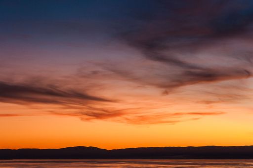 The beachside view of the orange-shaded sunset sky with red clouds