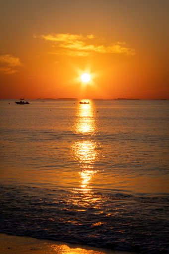 Sun rising over the ocean at the beach.  Boats in the water.