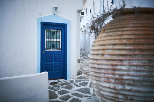 A beautiful shot of a white building with a blue door in the narrow street in Paros, Greece
