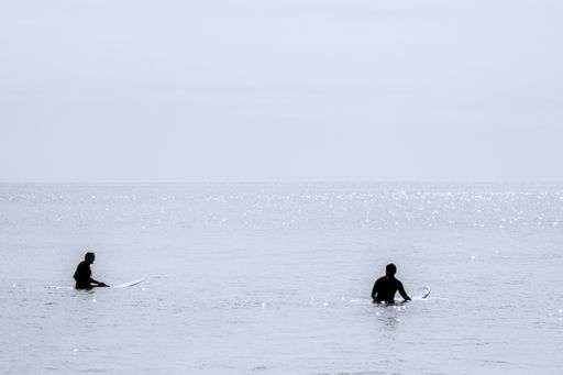 Two surfers waiting on a flat sea for a wave which may never come.