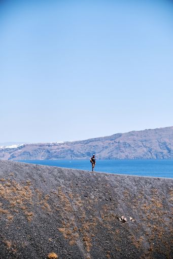 a vertical  shot of a lonely man standing on the edge of the volcano in Santorini, Greece