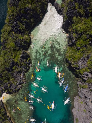 A vertical high angle shot of boats on a lake surrounded by moss covered rocky cliffs