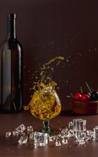 A glass of a splash wine on the table with ice, a bottle of wine and a fruit around it