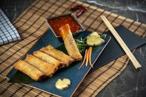 A high-angle view of Asian spring rolls and red sauce on the blue plate