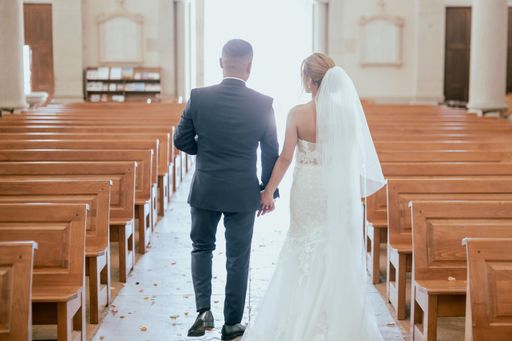 A selective focus of a wedding couple holding hands, walking down the church aisle