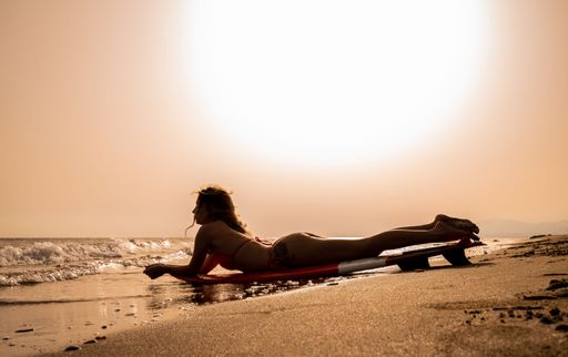 A Young woman with blonde hair walking on the beach with a surfboard on a sunny day