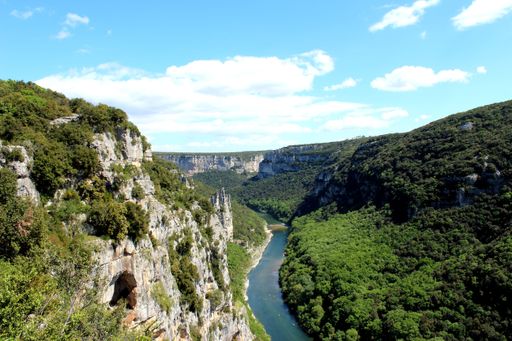 A view from a mountain top of a river between green mountains with vegetation under cloudy sky