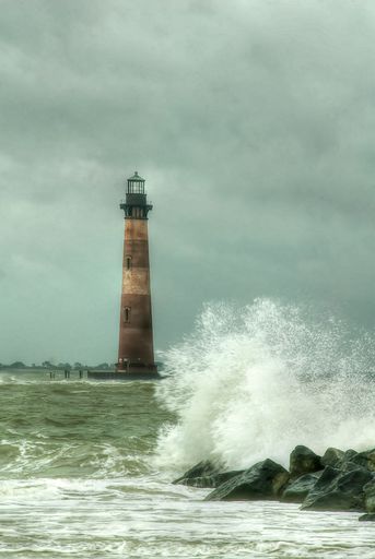 A vertical shot of an old lighthouse with waves crashing into rocks