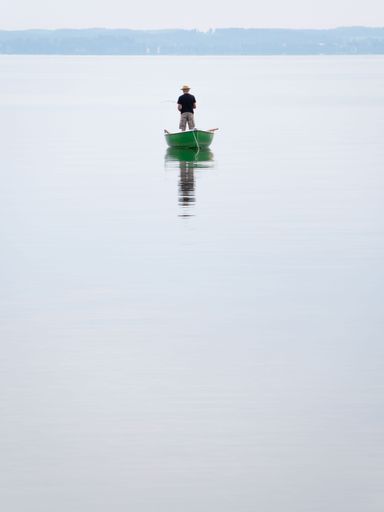 A minimalistic vertical shot of a man on the boat fishing on the lake